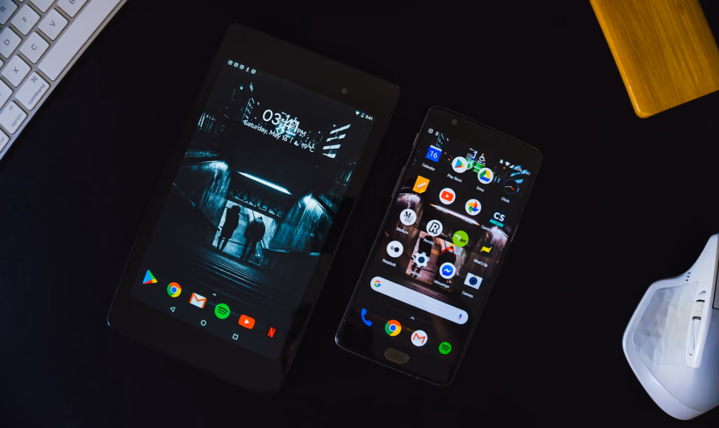 Two smartphones placed on a table beside a keyboard, showcasing a modern workspace setup.