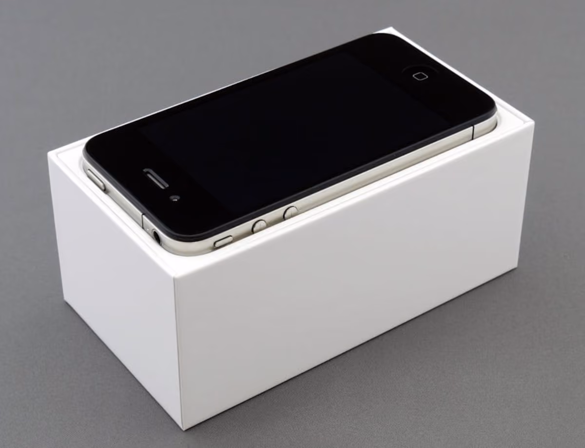 A white iPhone placed inside a box, resting on a gray surface, showcasing its sleek design and packaging.
