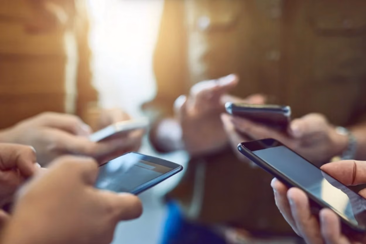 A group of individuals holding their cell phones, engaged in conversation or sharing information with one another.