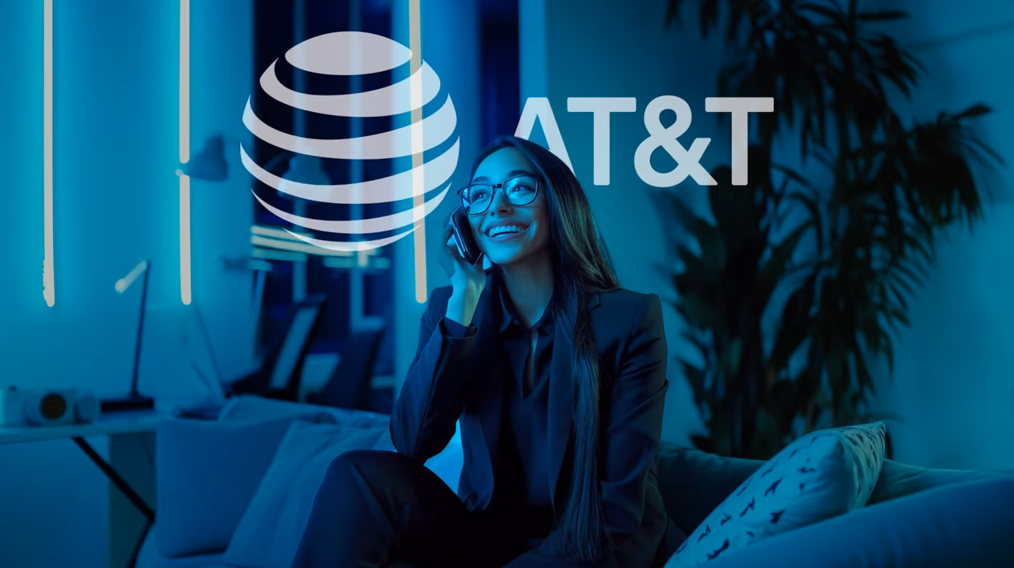A happy young woman with glasses and black suit, calling someone with her phone, appearing engaged with the content displayed, in her modern office room, blue vibes