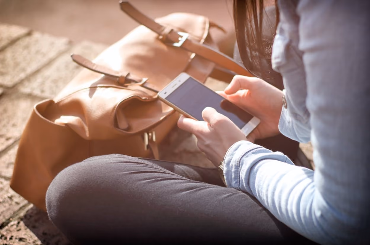 A woman seated on the ground, focused on her cell phone, with a serene expression on her face.
