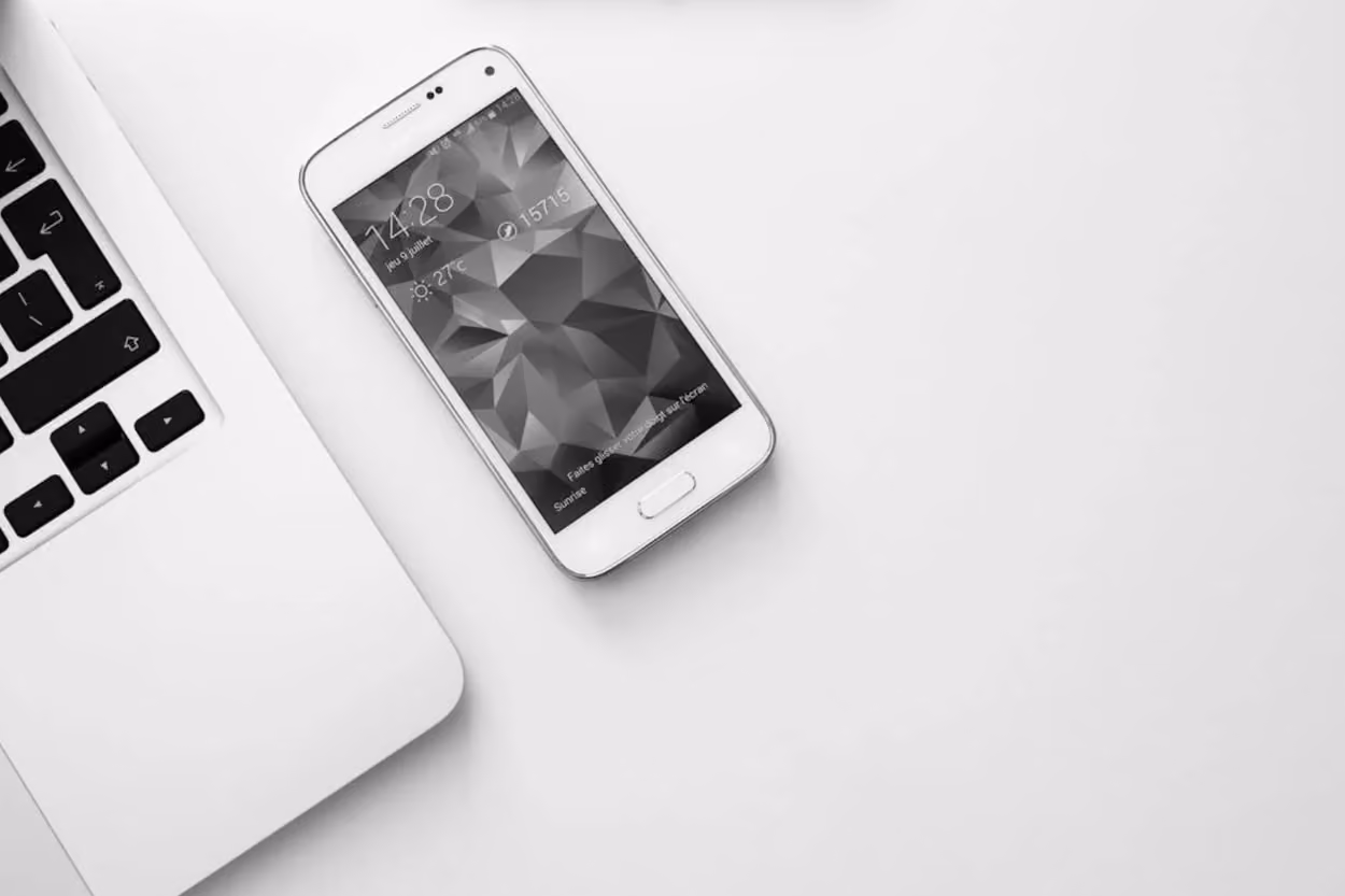 A smartphone, laptop, and a cup of coffee arranged neatly on a clean white surface.