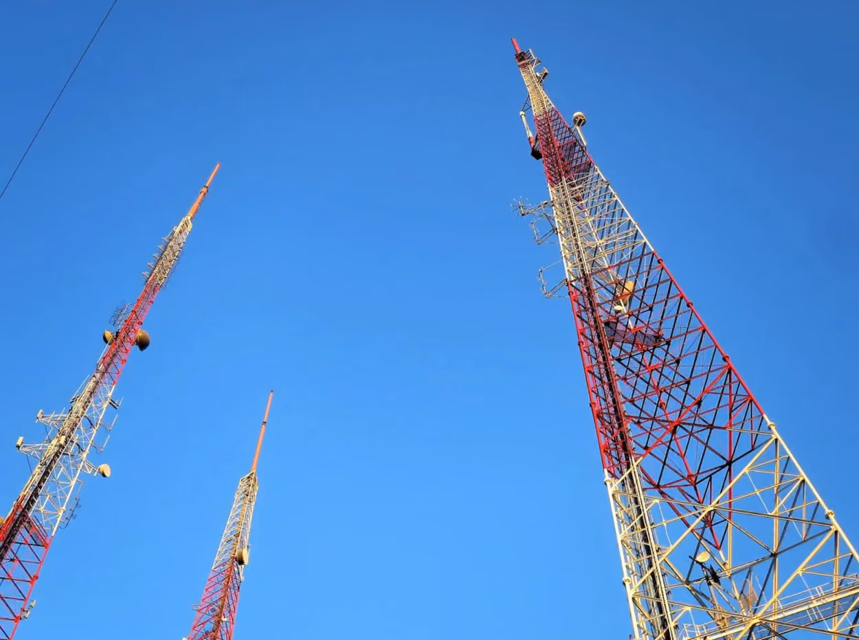 Three radio towers featuring red and white antennas against a clear sky, symbolizing communication technology.