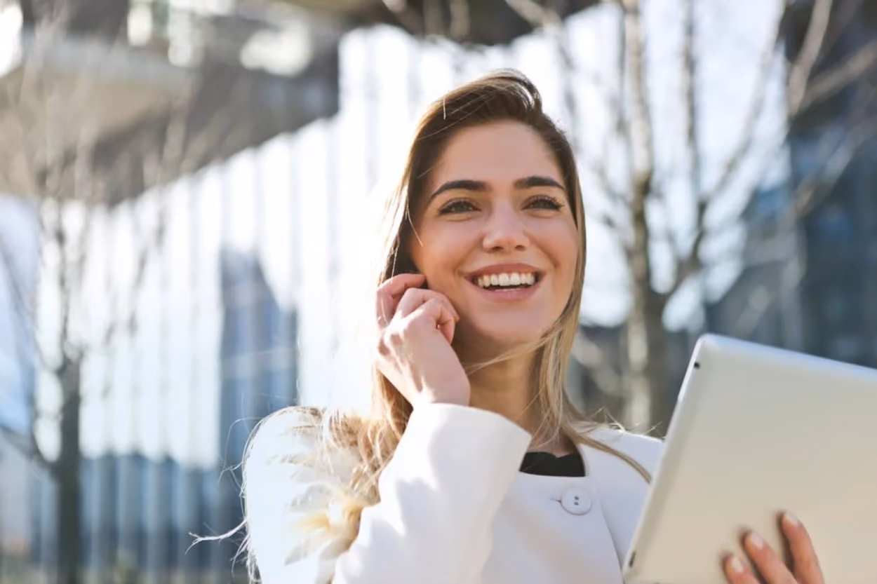A woman smiles brightly while holding a tablet computer in her hands, showcasing a moment of joy and engagement.