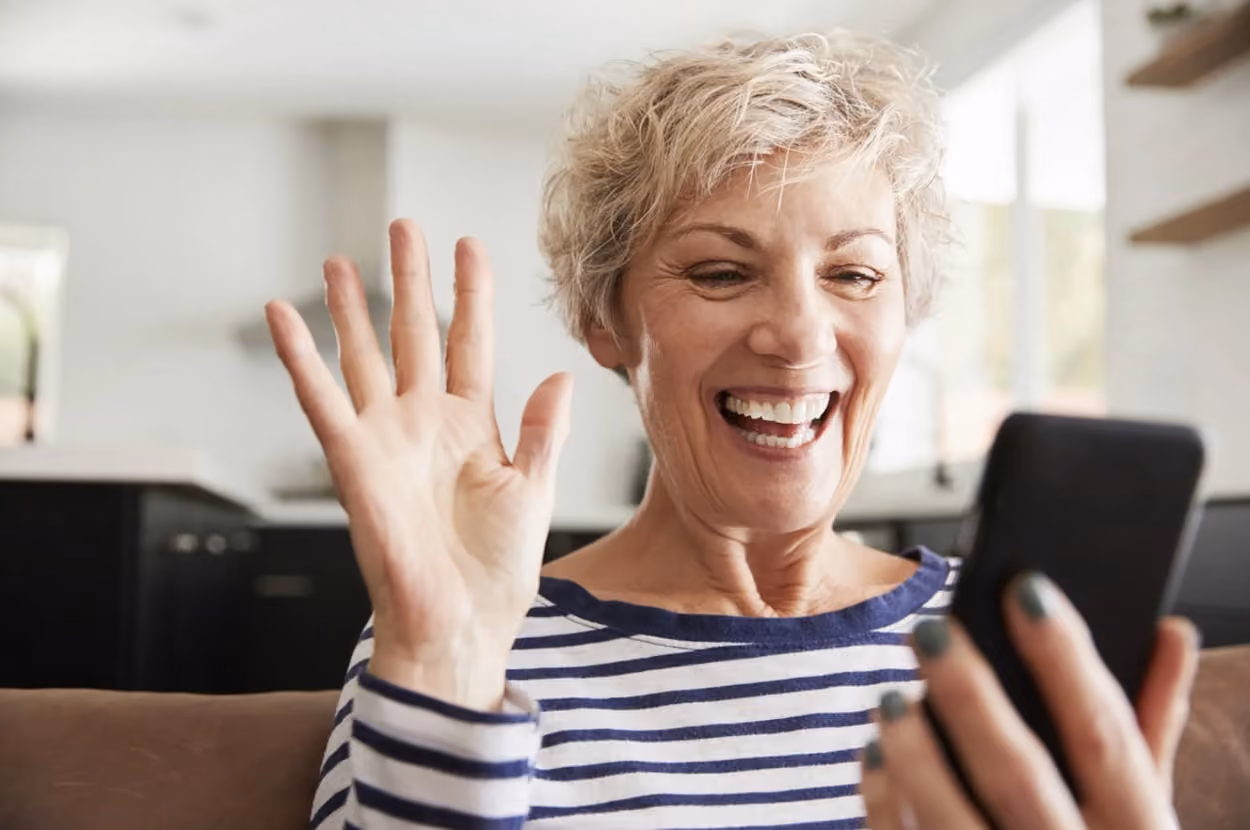 A woman smiles brightly while engaging with her phone, showcasing a moment of joy and connection.