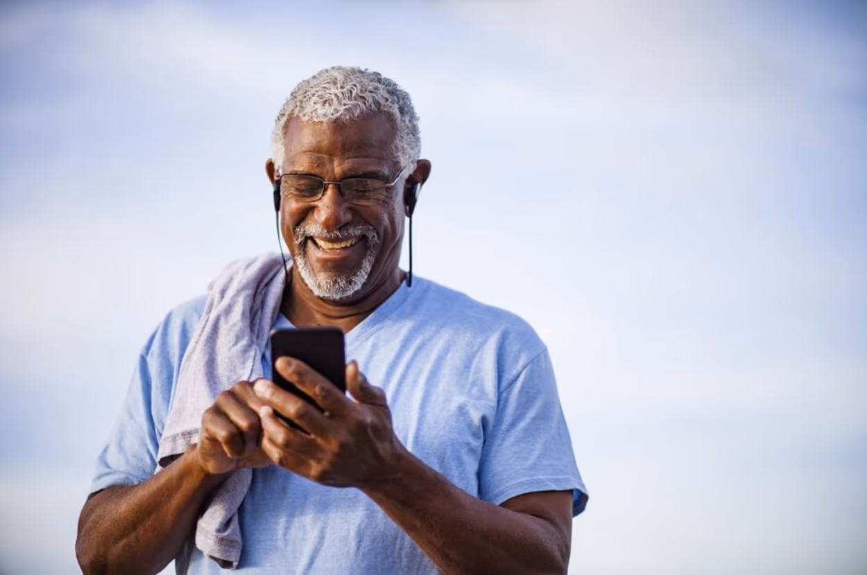 An older man walks while using his smartphone, focused on the screen as he navigates his surroundings.