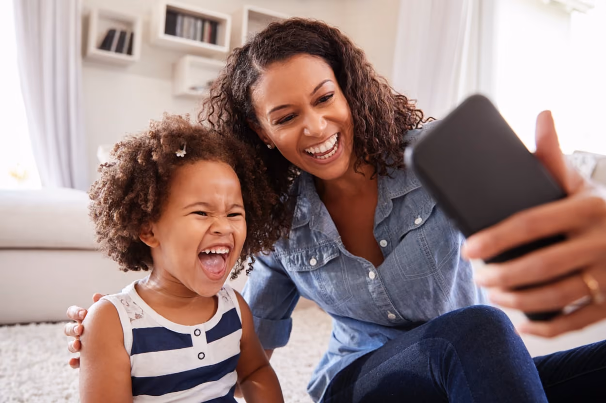 A woman and a child joyfully laughing together while capturing a selfie, showcasing their happy moment.
