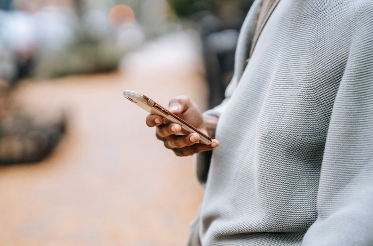 A man wearing a sweater is holding a cell phone, looking engaged in conversation or browsing content.
