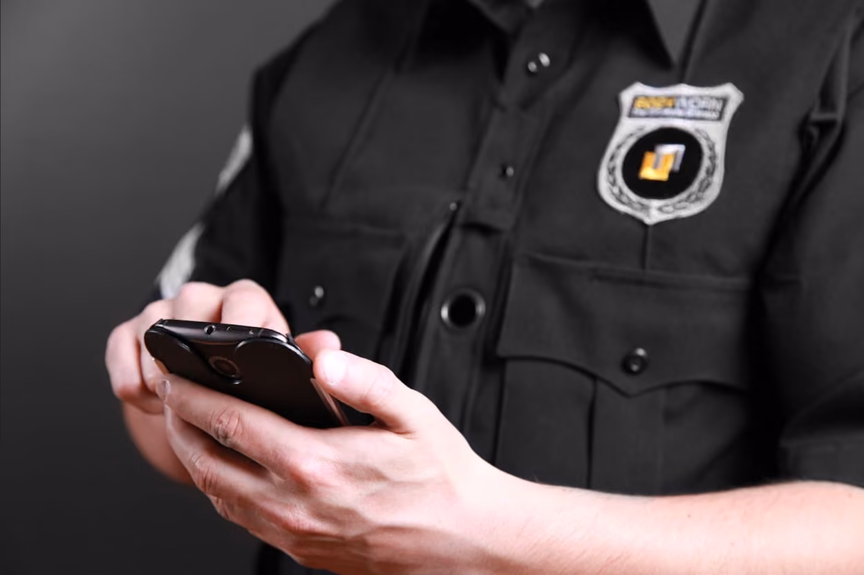 A police officer in uniform is holding a cell phone, appearing focused and engaged in communication.