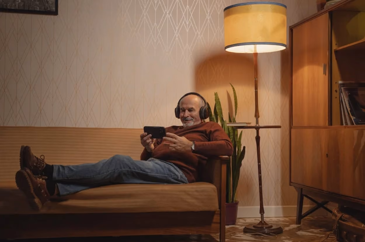 A man wearing headphones sits comfortably on a couch, immersed in his listening experience.