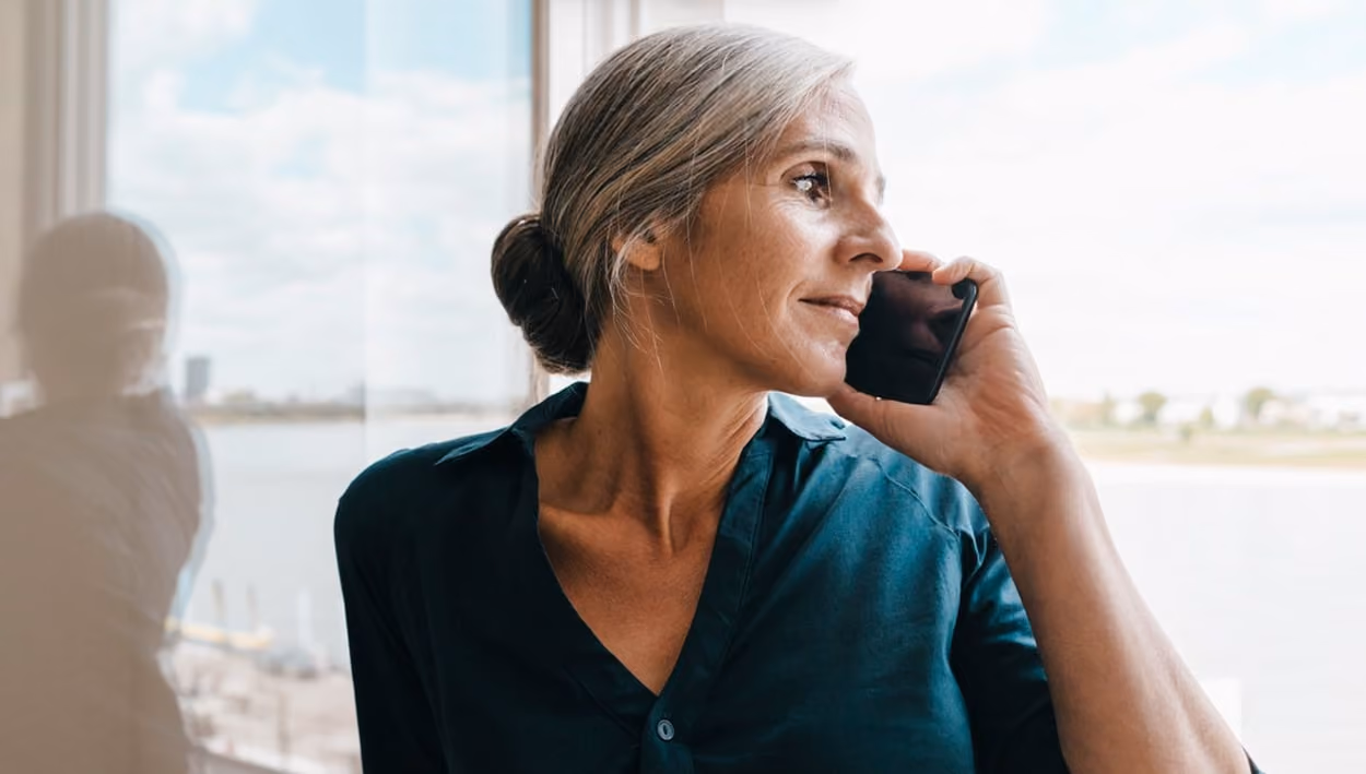 A woman converses on the phone, gazing thoughtfully out the window, capturing a moment of connection and reflection.