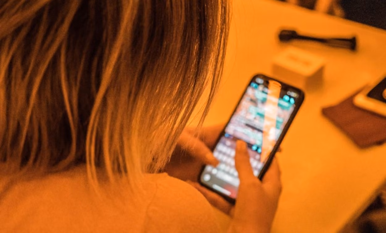 A woman seated at a table is engaged with her phone, focused on the screen in front of her.