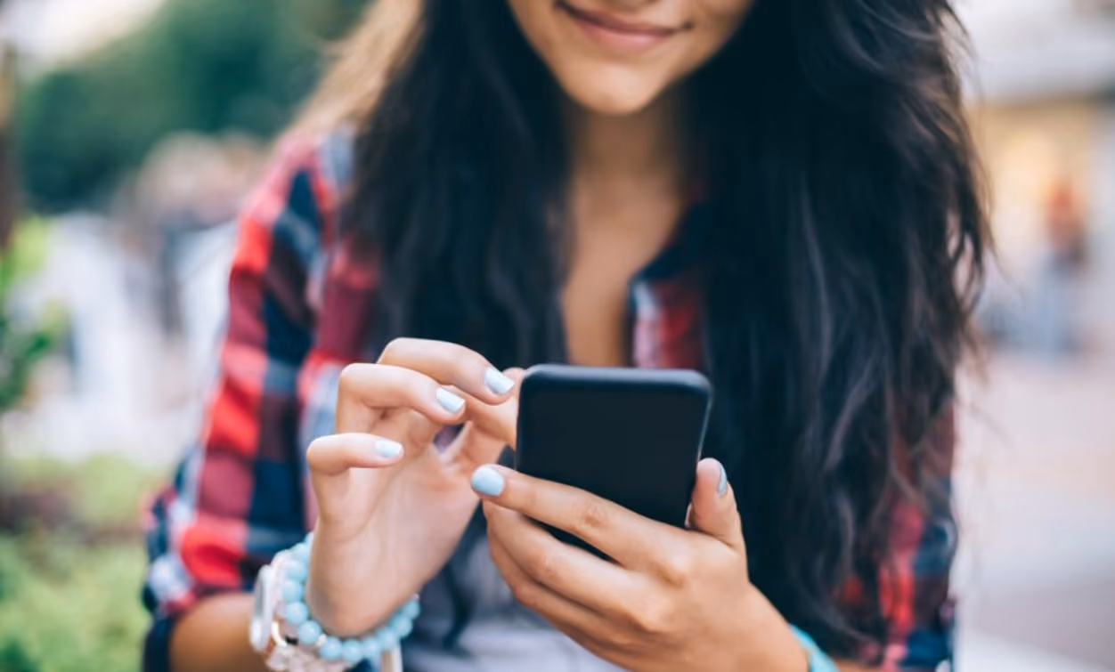 A woman smiles brightly as she engages with her cell phone, radiating joy and connection in her expression.