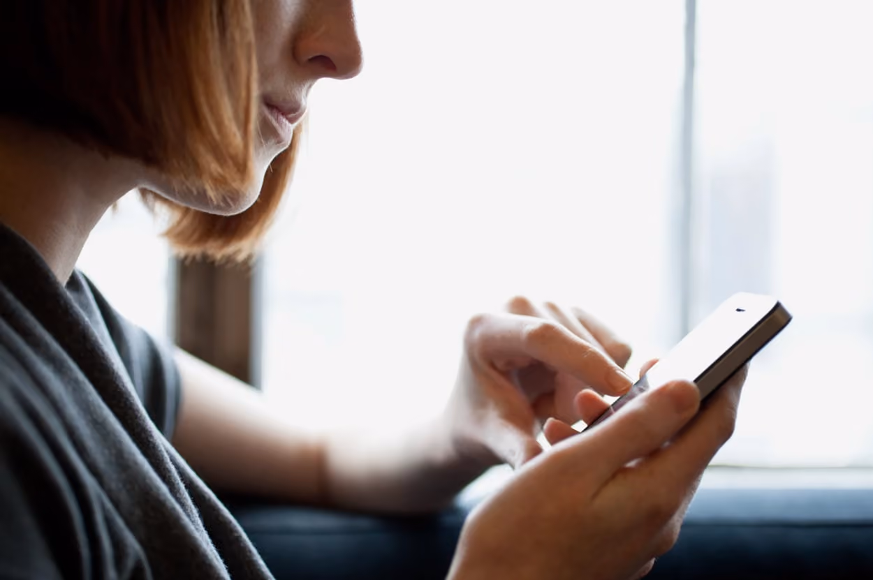 A woman is engaged with her cell phone, focused on the screen while sitting in a casual environment.