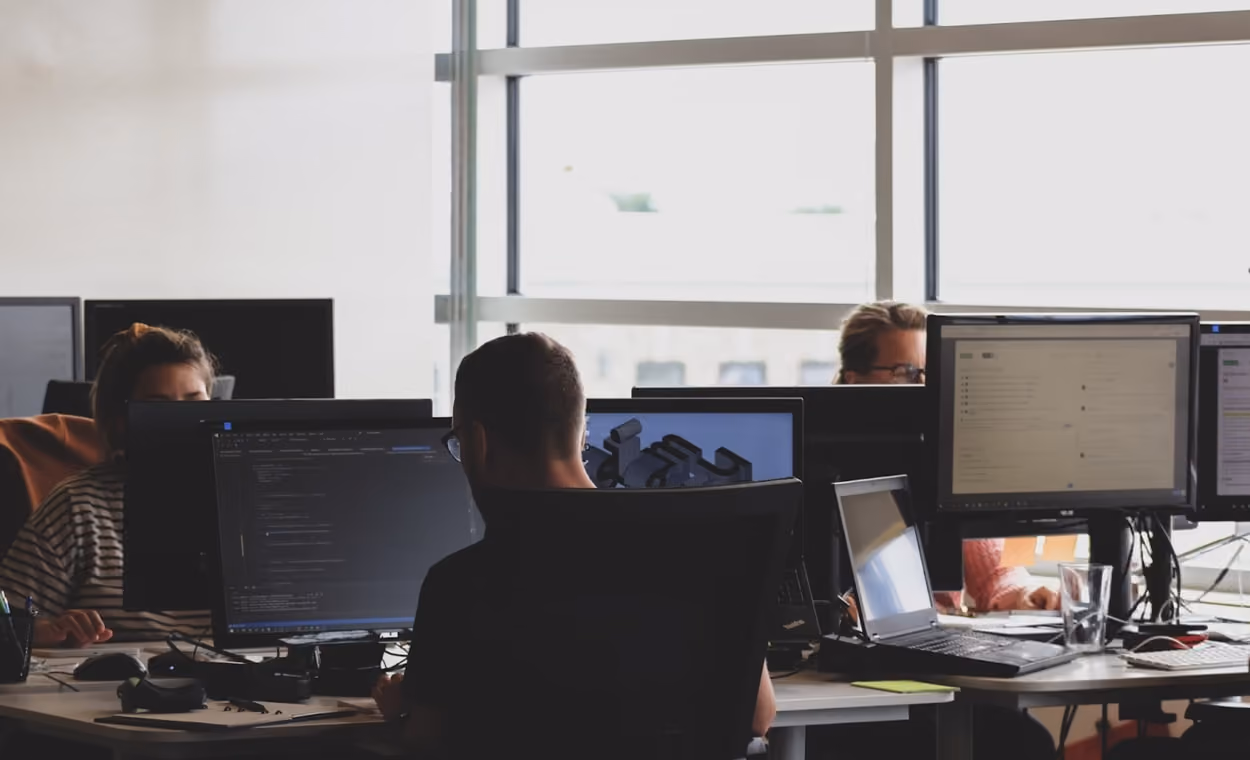 A group of professionals focused on their computers in a modern office environment, collaborating on various tasks.