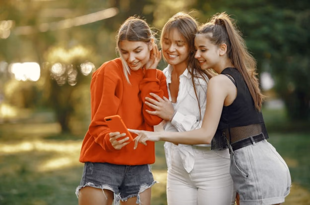 Three young women gathered together, intently looking at a cell phone, sharing a moment of engagement and conversation.