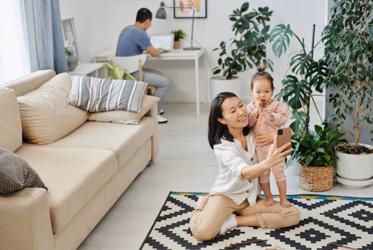 A woman and a child sit on the floor of a cozy living room, surrounded by soft furnishings and warm lighting.