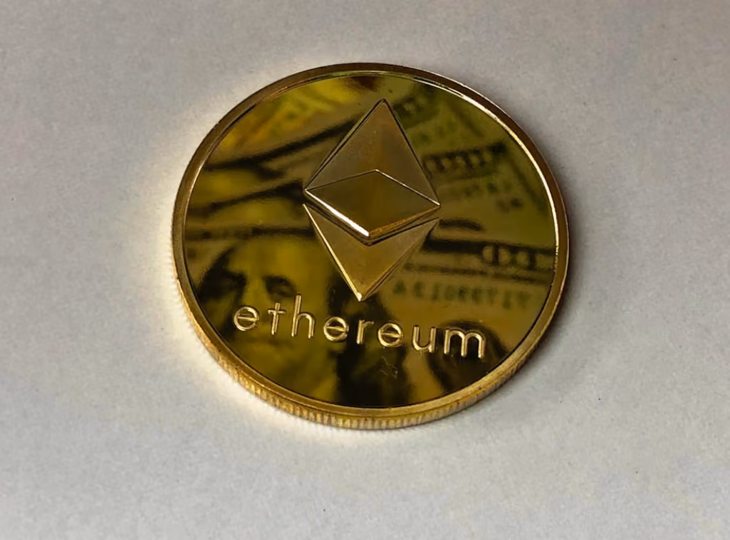 Ethereum coin resting on a white surface, showcasing its distinctive logo and metallic finish.  