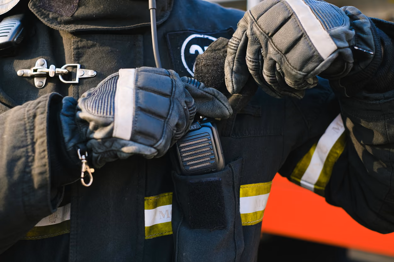 A firefighter in gloves and a helmet stands ready for action, showcasing their protective gear and commitment to safety.