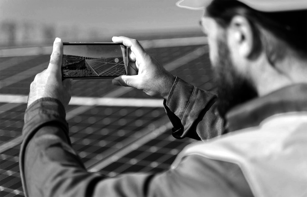 A man photographing solar panels with his smartphone, capturing renewable energy technology in action. 