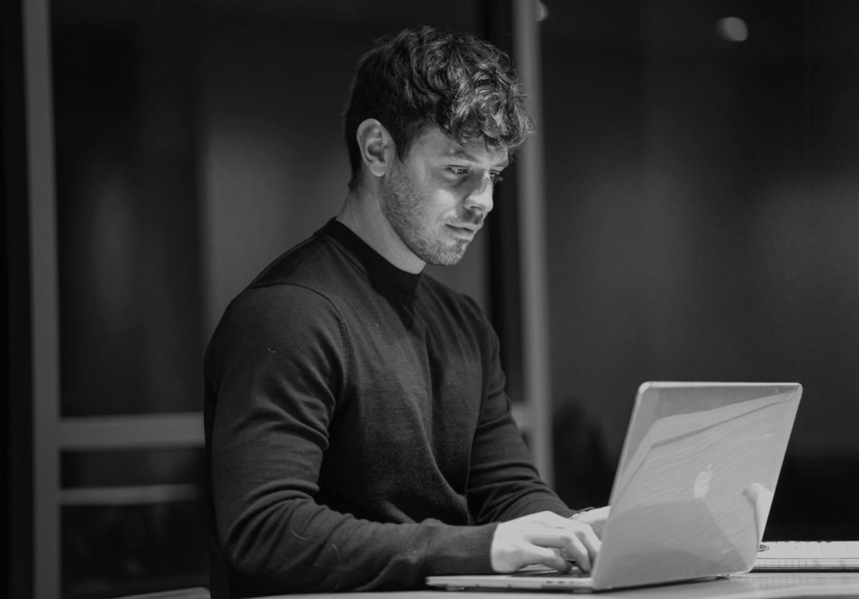 A man at a table using a laptop, concentrating on the screen in front of him.