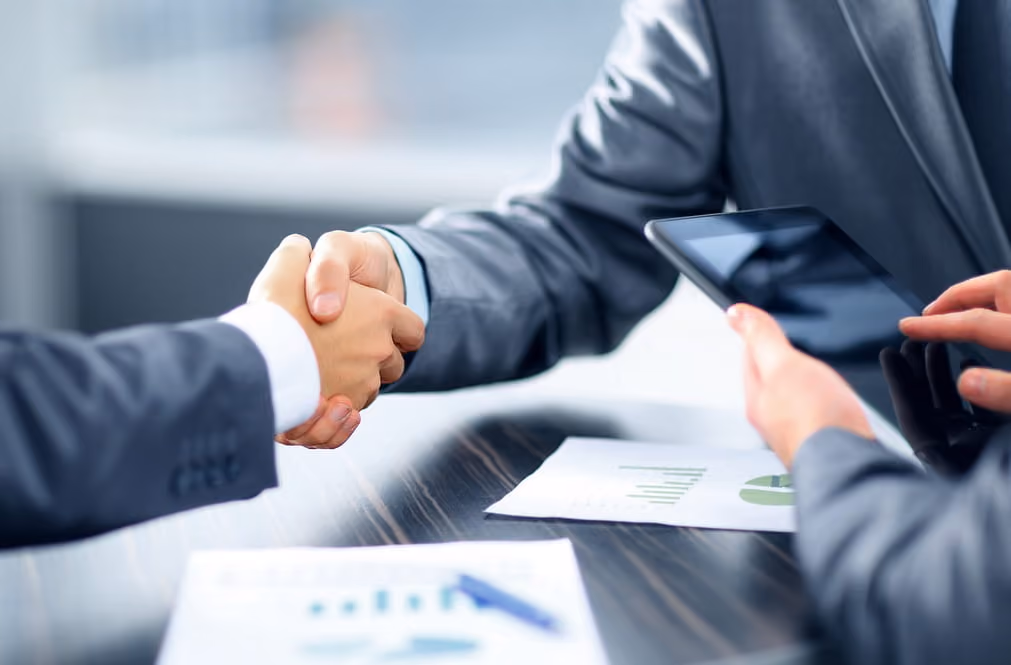 Business professionals shaking hands over a conference table, symbolizing agreement and collaboration.