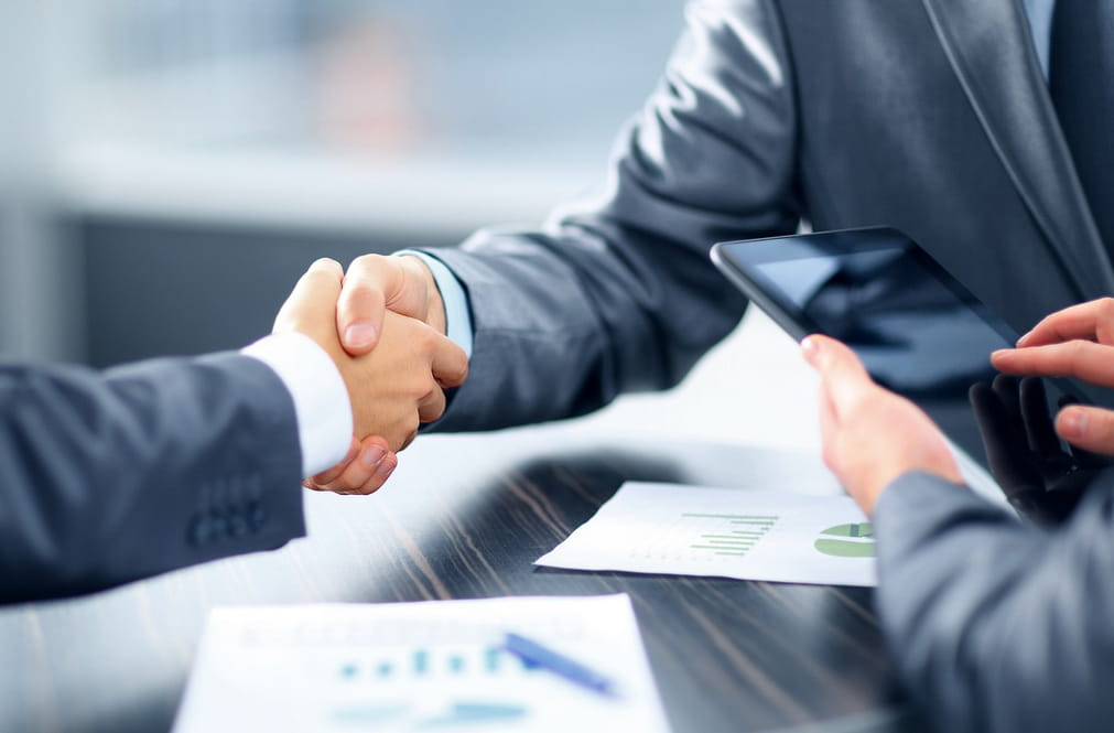 Business professionals shaking hands over a conference table, symbolizing agreement and collaboration.