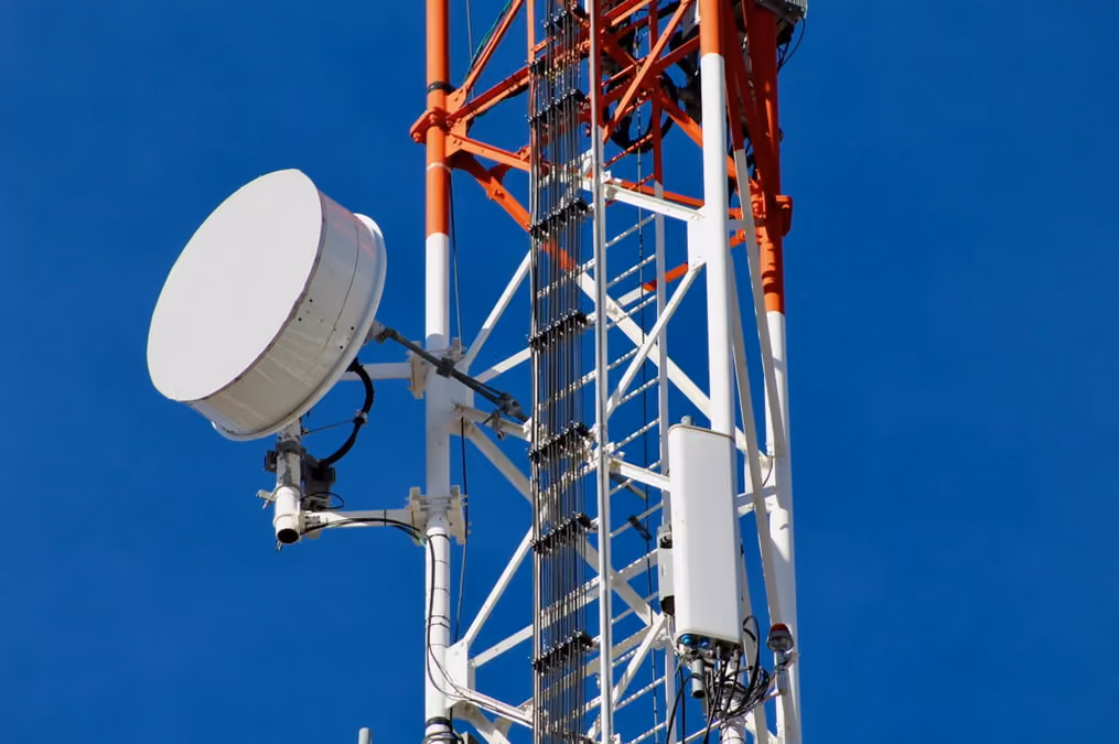 Cellular tower featuring a satellite dish and multiple antennas against a clear blue sky.