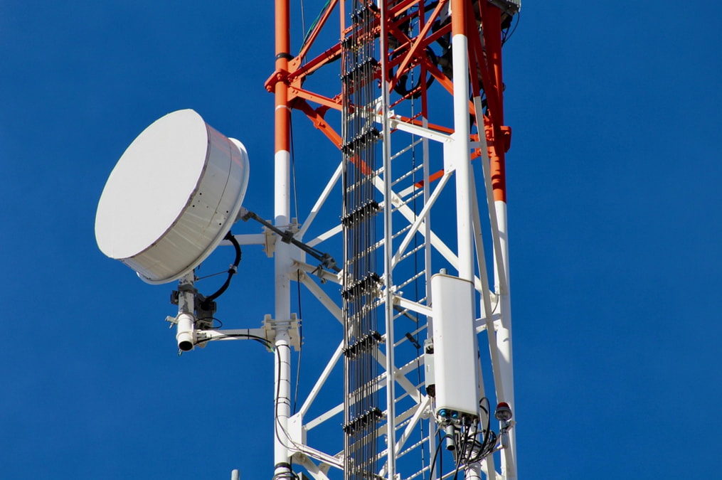Cellular tower featuring a satellite dish and multiple antennas against a clear blue sky.