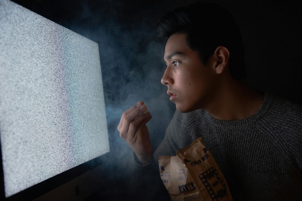 A man stares at a television screen emitting smoke, indicating a possible malfunction or fire hazard.