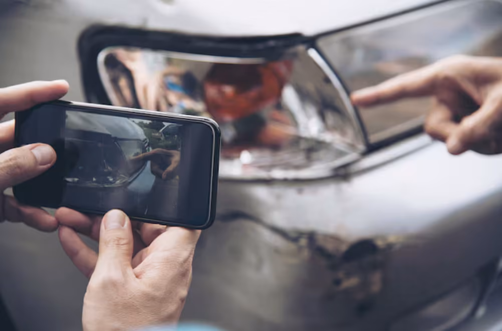 A person photographing a damaged car, capturing the extent of the vehicle's injuries after an accident.