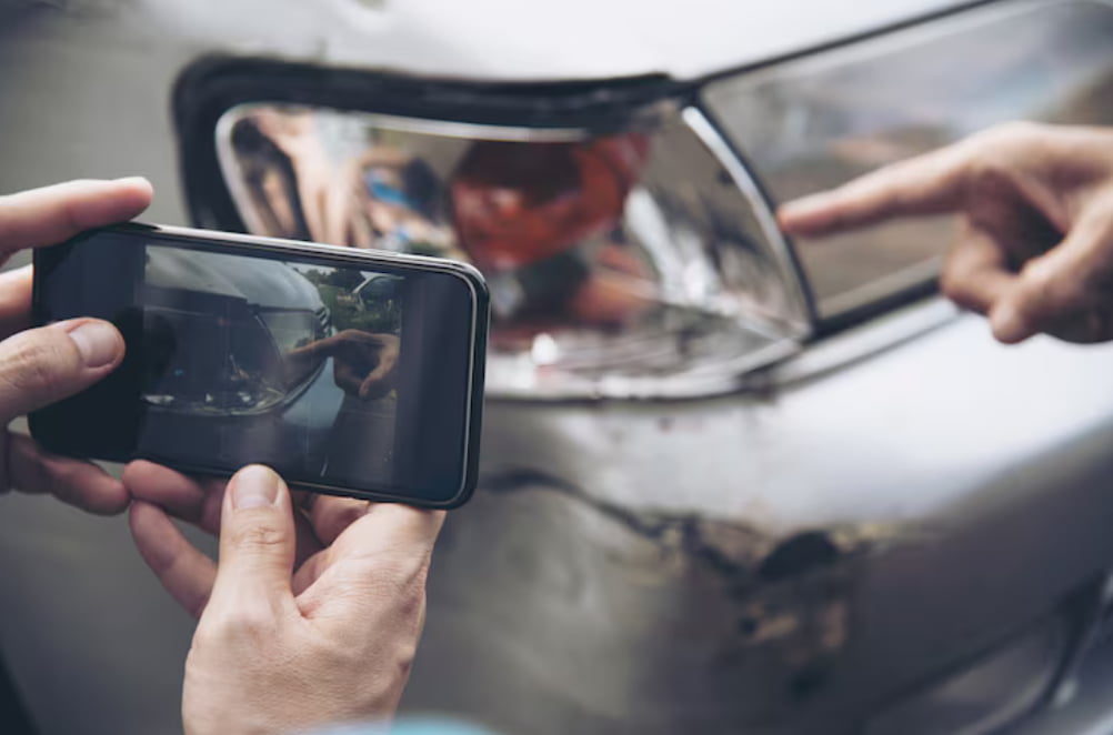A person photographing a damaged car, capturing the extent of the vehicle's injuries after an accident.