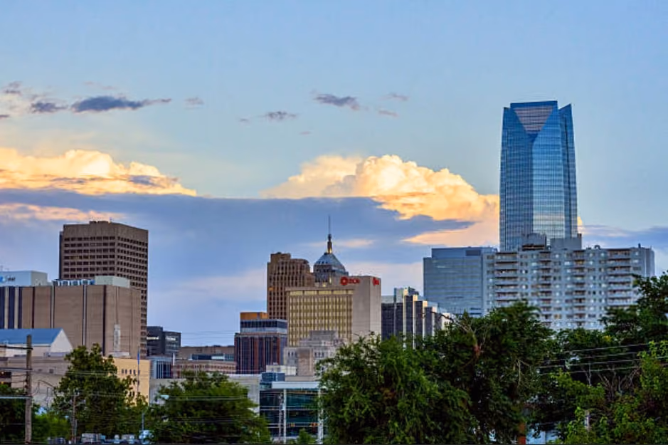 City skyline featuring tall buildings and greenery from trees in the foreground.