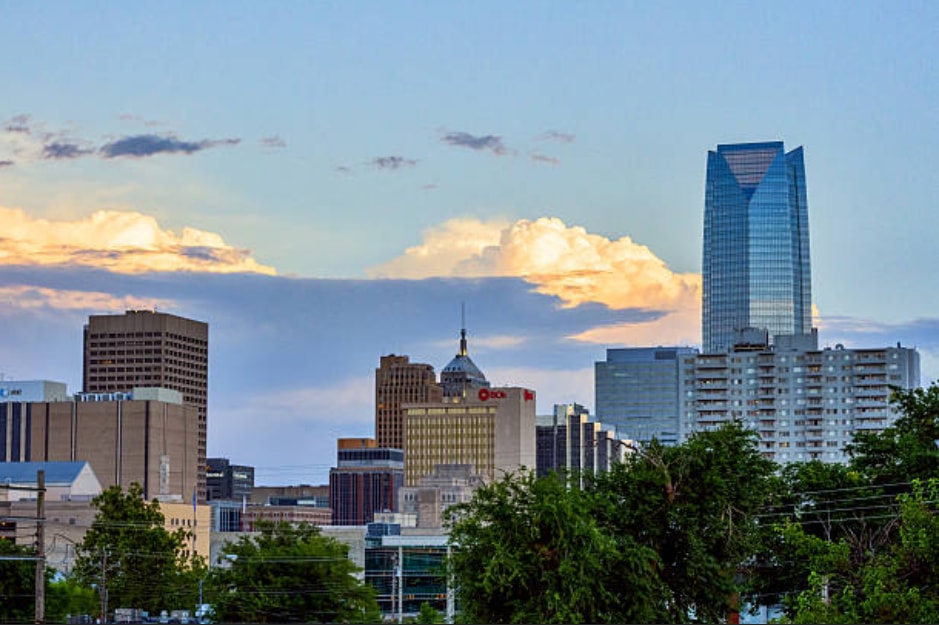 City skyline featuring tall buildings and greenery from trees in the foreground.  