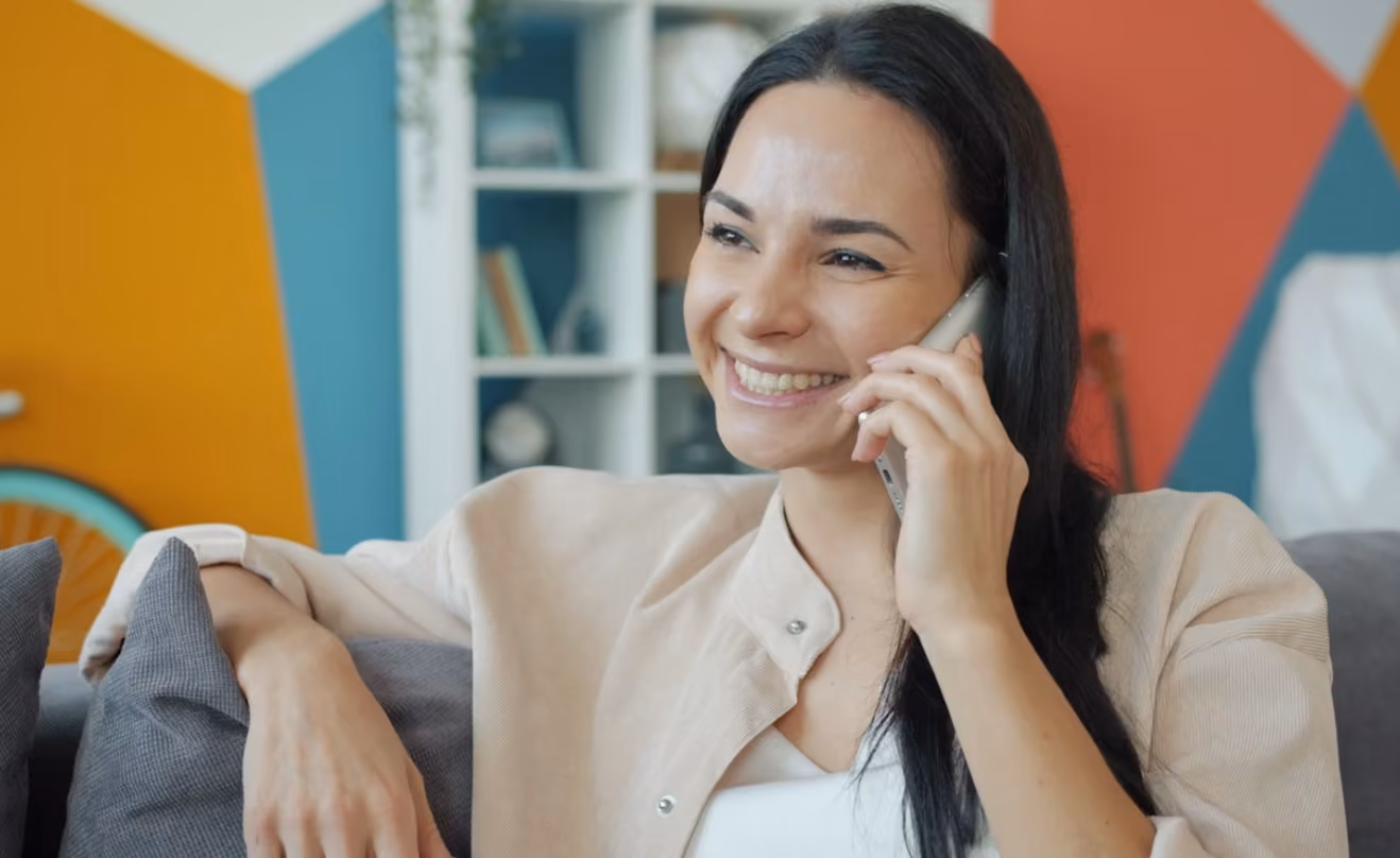 A woman with a cheerful expression speaks on her cell phone, indicating a pleasant interaction.