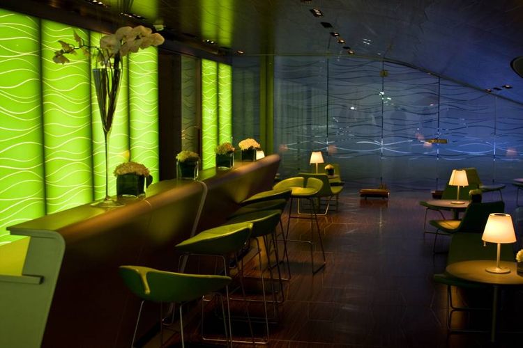 Intérieur contemporain de café-bar avec éclairage vert, sièges modernes et petites lampes sur les tables.