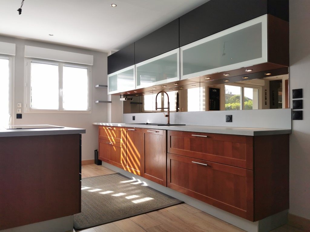 Cuisine moderne avec armoires en bois foncé, plans de travail gris et grandes fenêtres lumineuses.