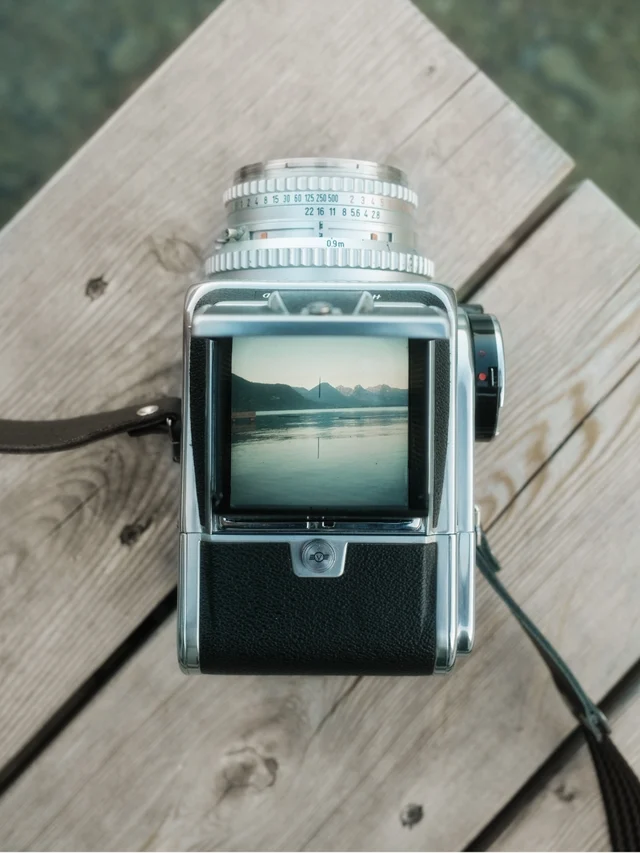 Top view of a vintage medium format camera displaying a lake and mountain scene reflected on its viewfinder, placed on wooden planks.