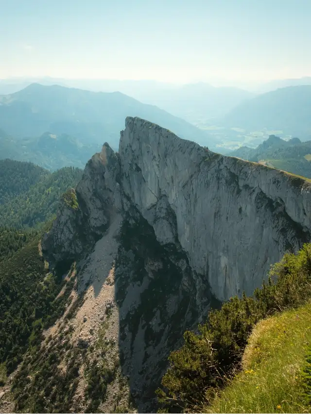 Steep rocky mountain ridge surrounded by forested slopes under a clear sky.