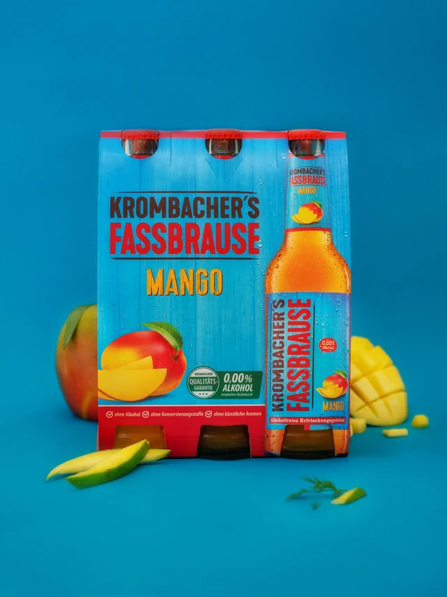 Pack of Krombacher's Fassbrause Mango beverage with a bottle and mango fruit slices on a blue background.