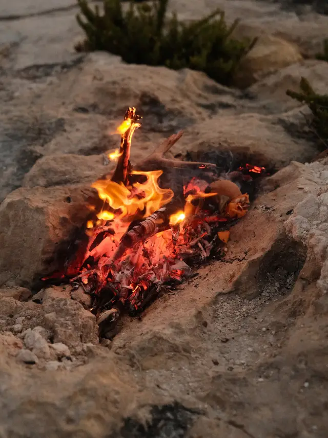 Small campfire burning with glowing embers and flames among rocks outdoors.