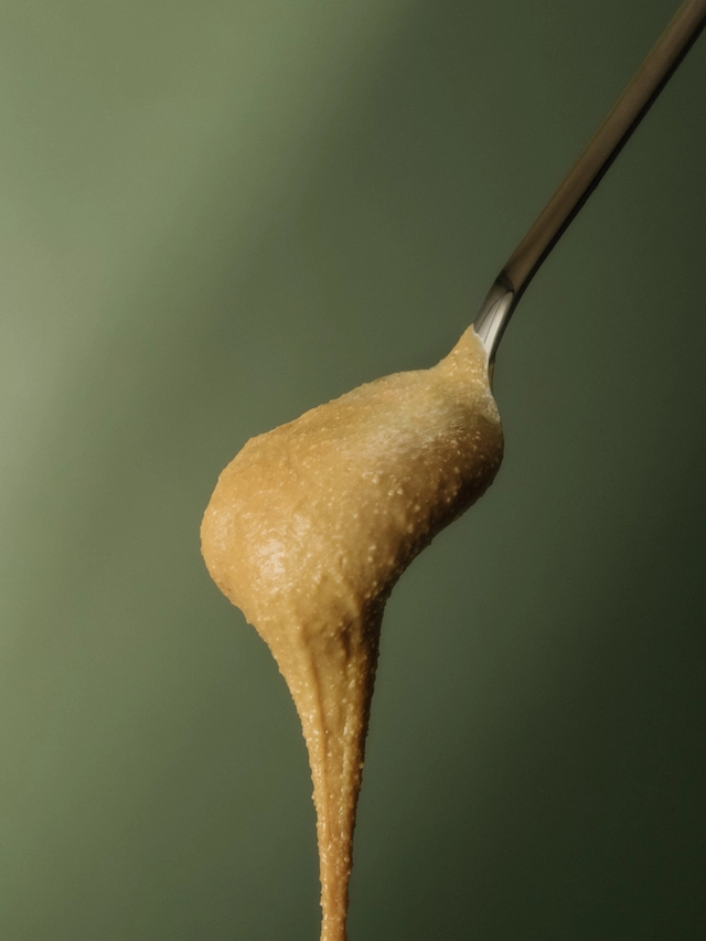 A spoonful of thick, creamy peanut butter dripping against a green background.