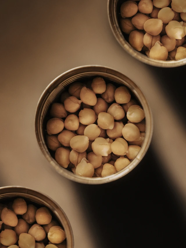 Top view of three open metal cans filled with beige chickpeas on a brown surface.