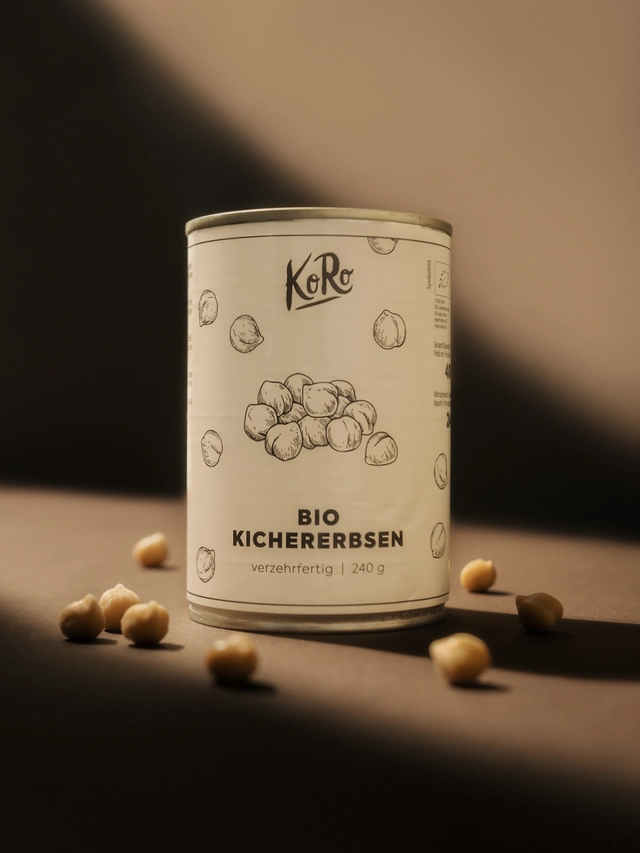 Tin can of KoRo brand organic chickpeas with scattered chickpeas on a brown surface.