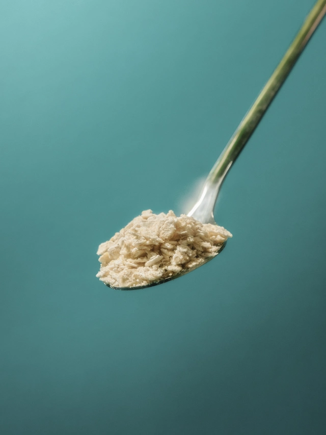 Silver spoon holding a scoop of beige powdered supplement against a teal background.