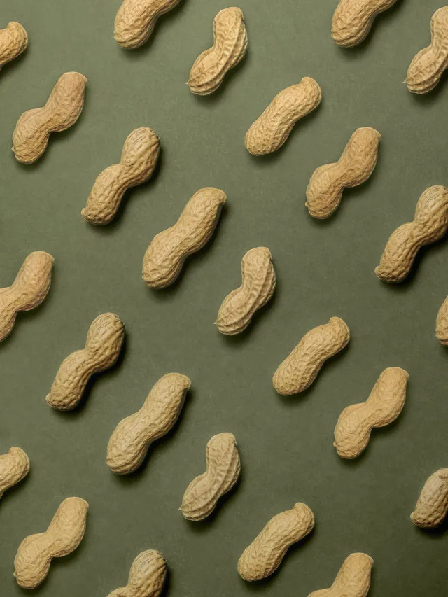 Pattern of whole unshelled peanuts arranged diagonally on a green background.