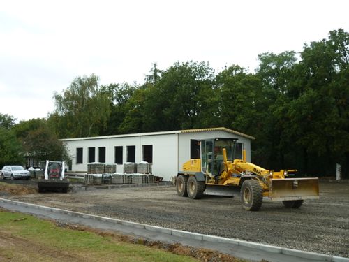 Pohled na výstavbu hangáru s betonovou podlahou a stojánkou se stavebními stroji.