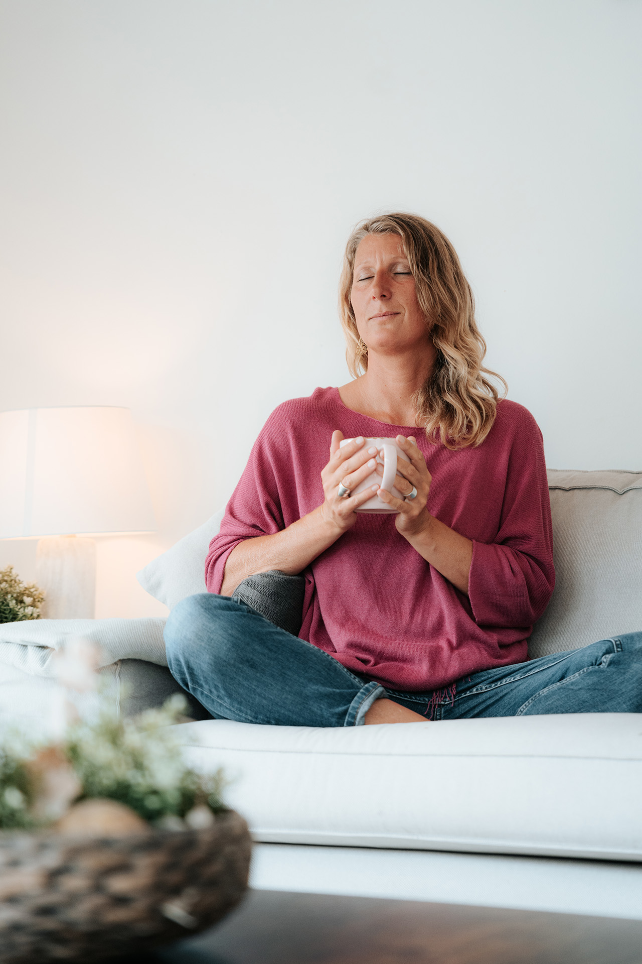 Burnout-Coach Martina Knall sitzt mit geschlossenen Augen auf dem Sofa und hält eine Tasse – Symbol für Selbstfürsorge, Ruhe und Regeneration nach Burnout.