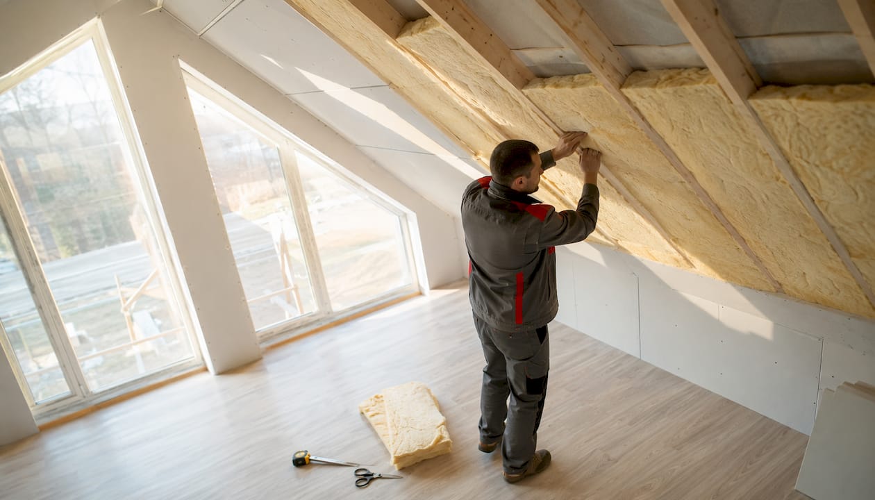 Ein Handwerker bringt Dämmmatten zwischen den Sparren im Dachgeschoss an.