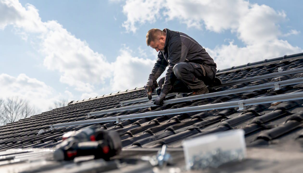 Ein Dachdecker montiert die Unterkonstruktion für die Photovoltaikanlage auf dem Dach.